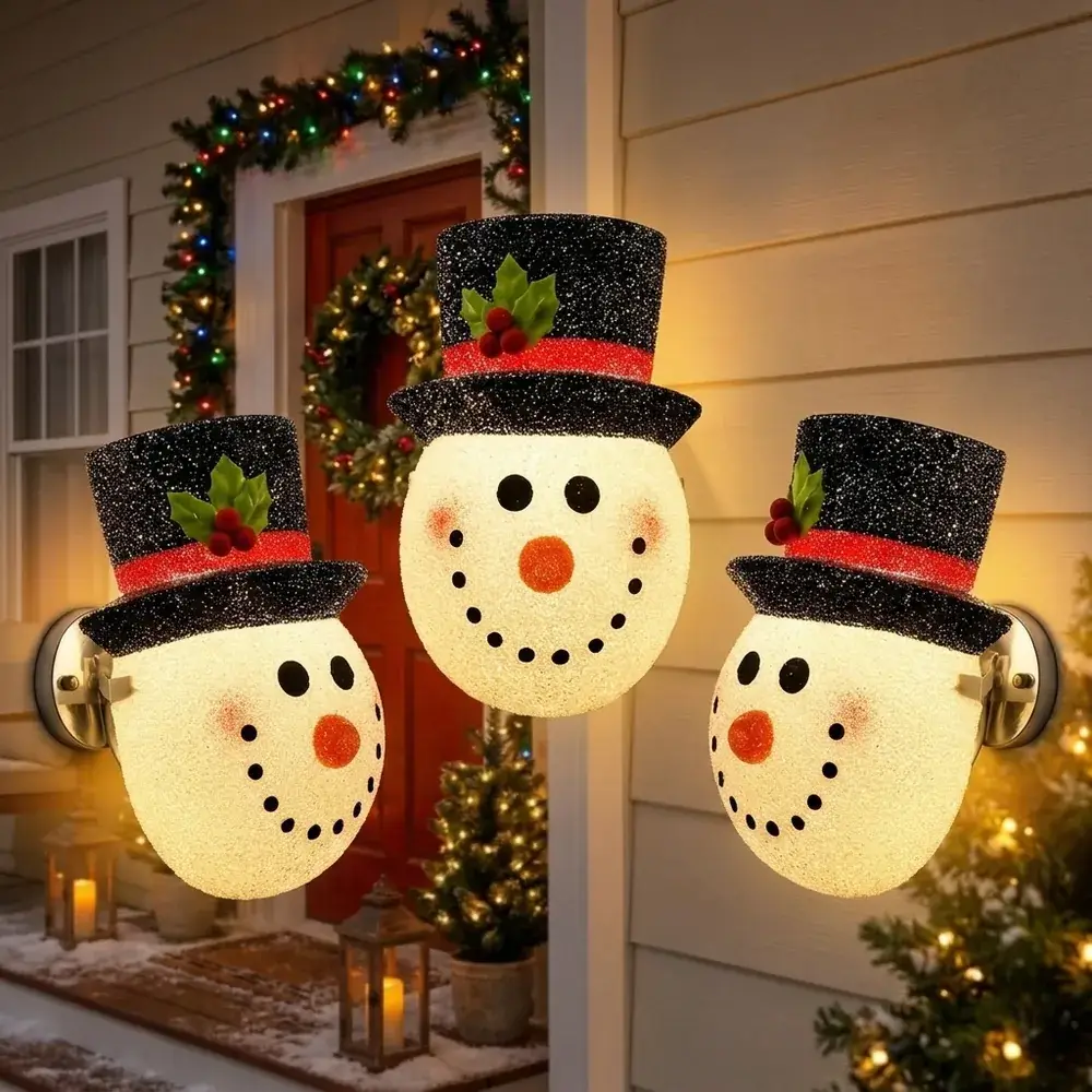Três bonecos de neve luminosos acesos, dispostos em arco à frente de uma entrada decorada para o Natal