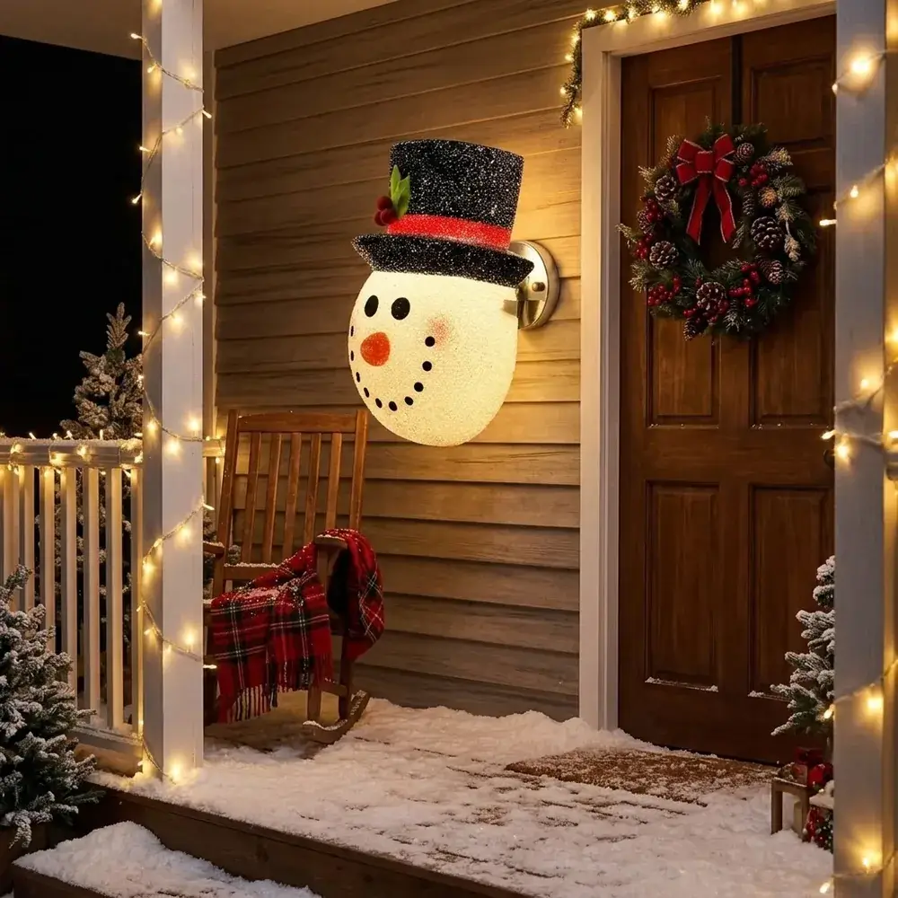 Alpendre com neve à noite e o boneco de neve a brilhar no candeeiro junto à porta